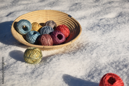 Korb mit Wollknäuel aus Seide in verschiedenen Farben auf frischem Schnee