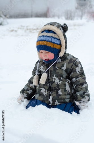 Little boy playing in the snow on the street. Kid with red cheeks in the snow
