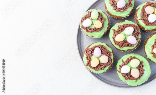 Carrot cupcakes with cream cheese frosting and Easter chocolate eggs, on gray plate, horizontal, copy space, top view