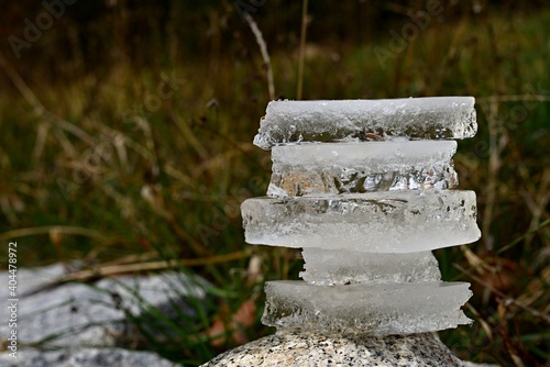 Ice stacked on top of each other. Balancing ice pieces into an mound. Pieces of ice stacked on a large boulder with winter green-brown grass in the background. Romantic view of ice in nature.