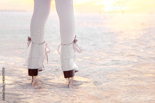 Legs of little girl skating on ice in evening sunset light. Winter sports on natural background.