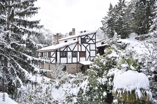 Postcard photo with white house with wooden sleepers on the facade, sundial, trees around. All covered by snow after the passage of the Filomena snowstorm in Spain, January 2021. photo