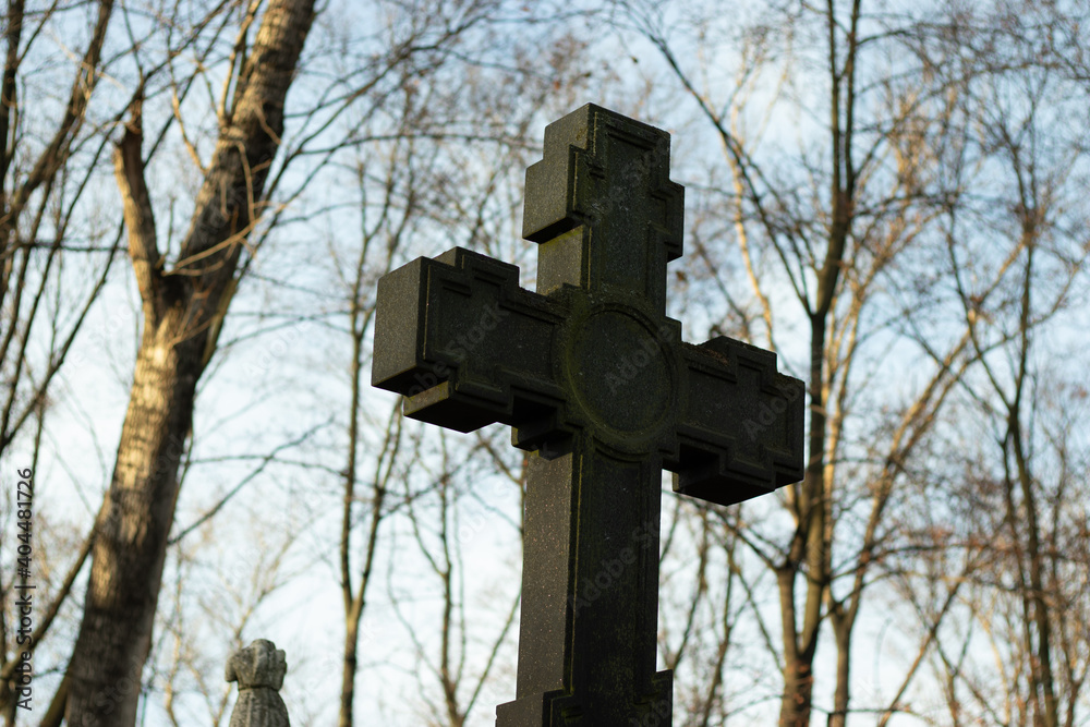 Large Christian cross made of dark stone against the background of tree branches and sky. Religion concept Large Christian cross made of dark stone against the background of tree branches and sky. Religion concept