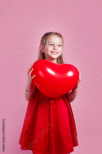 Valentines day. Little girl in red dress with heart shape air balloon on pink background © Elena Kratovich