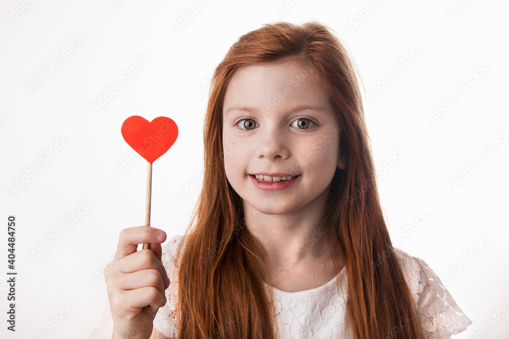Portrait of smiling red-haired caucasian little girl holding red heart on stick in her hand. Love, Valentines Day, Mothers Day, Fathers Day or happy birthday concept. Portrait of smiling red-haired caucasian little girl holding red heart on stick in her hand. Love, Valentines Day, Mothers Day, Fathers Day or happy birthday concept.