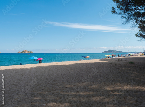 view of sand beach Spiaggia di Santa Maria Navarrese, sea with colorful beach umbrella and sunbeds and view of Arbatax penisula. Summer sunny day, Sardinia, Italy