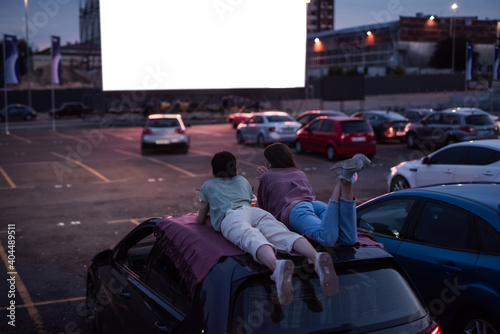 Come here and watch. Rear view of two friends lying on the roof of a car, having fun while watching a movie in an open air cinema photo