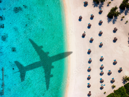 Travel concept with an airplane shadow flying towards a tropical beach with coconut palm trees and turquoise sea