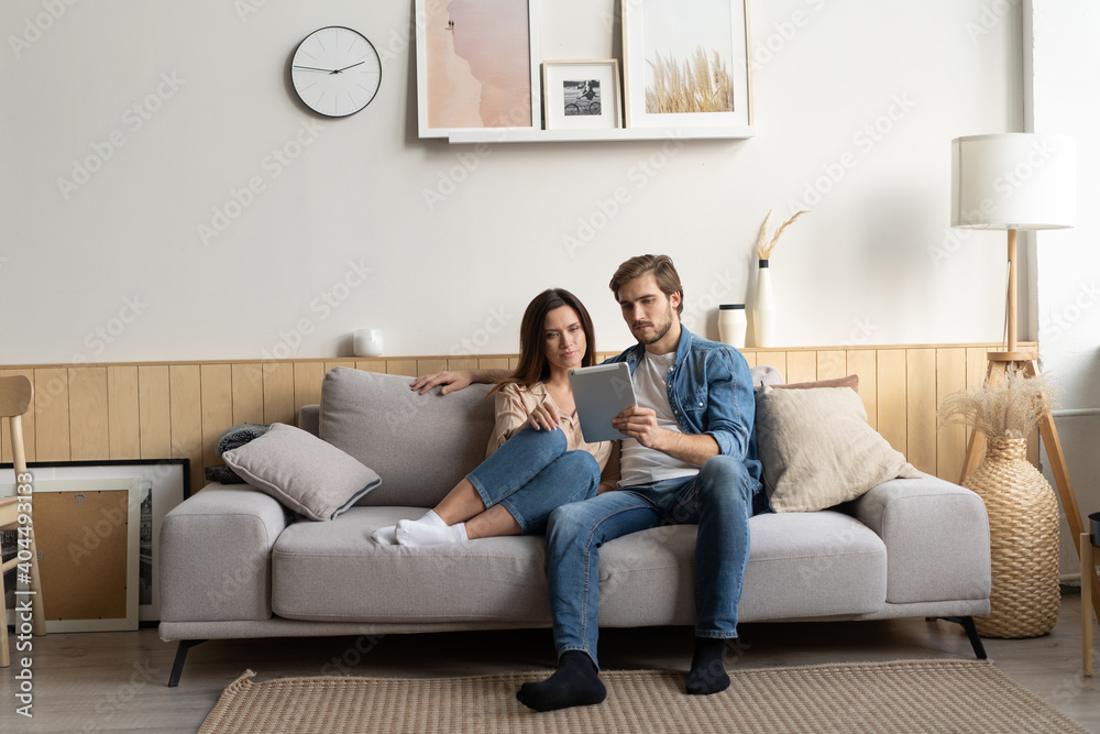 Young couple sitting on couch at home, using a tablet PC for Internet and social media. Young couple sitting on couch at home, using a tablet PC for Internet and social media.