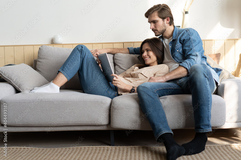 Young couple sitting on couch at home, using a tablet PC for Internet and social media.