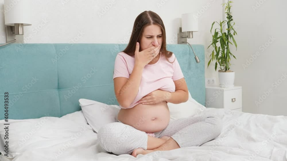 Pregnant woman feeling sick with nausesa sitting on bed at morning. Intoxication during pregnancy Pregnant woman feeling sick with nausesa sitting on bed at morning. Intoxication during pregnancy