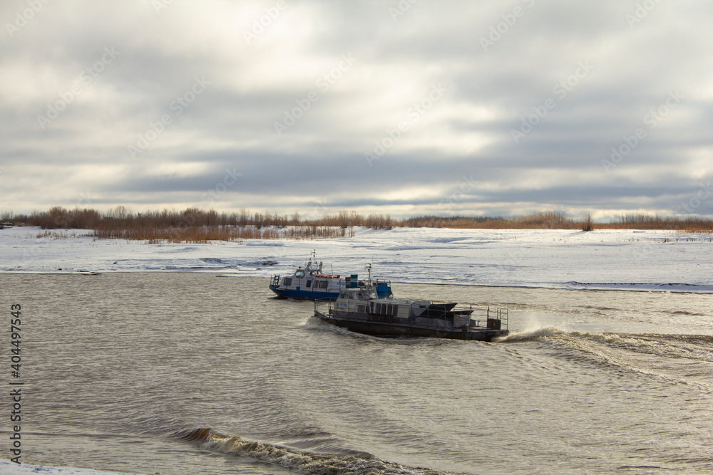 Two ships sail along the channel of the northern river. At the beginning of winter, two ships sail along a narrow channel among the banks covered with snow. Two ships sail along the channel of the northern river. At the beginning of winter, two ships sail along a narrow channel among the banks covered with snow.