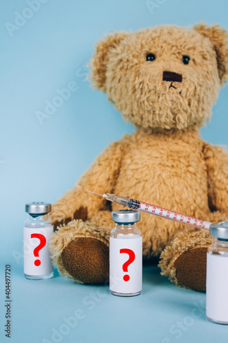 Vertical image of teddy bear with unnamed vial dose of vaccine or another medicine with syringe against blue background with copy space - vaccine hesitancy or anti-vax concept. Selective focus photo