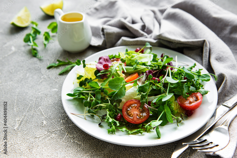 Fresh green mixed salad bowl with tomatoes and microgreens on concrete background. Healthy food, top view. Fresh green mixed salad bowl with tomatoes and microgreens on concrete background. Healthy food, top view.