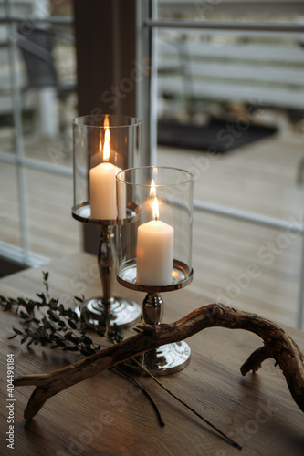 two candles and dry wood
on a table with a white tablecloth against the background of a window