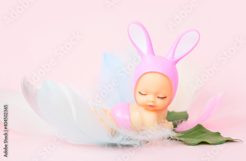small baby doll with rabbit ears and painted eggs on a pink background, the concept of a greeting card for Easter