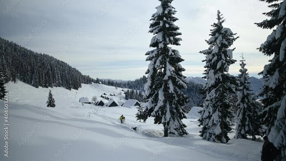 People walking on snowy landscape in Slovenia. Beautiful Alpine settlement covered in snow. Spruce trees growing on Pokljuka plateau. Zajamniki village in winter season. Static shot, real time People walking on snowy landscape in Slovenia. Beautiful Alpine settlement covered in snow. Spruce trees growing on Pokljuka plateau. Zajamniki village in winter season. Static shot, real time
