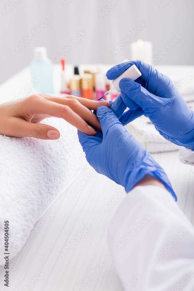 Obraz premium cropped view of manicurist in latex gloves applying nail polish while making manicure to client