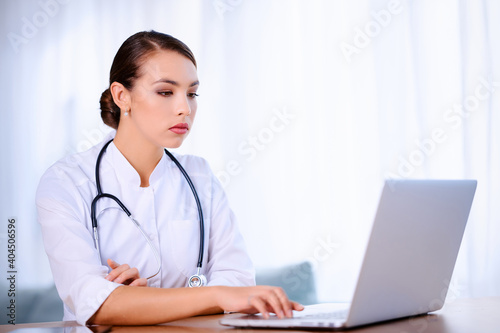 Female doctor with stethoscope wearing laboratory coat works in hospital and using laptop