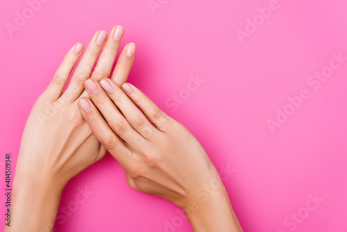 top view of female hands with pastel nail polish on fingernails on pink background