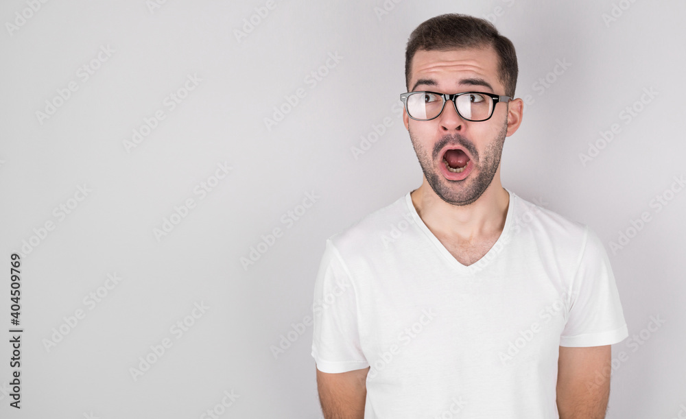 Surprised man with glasses in a white t-shirt looking to the side on a gray background Surprised man with glasses in a white t-shirt looking to the side on a gray background
