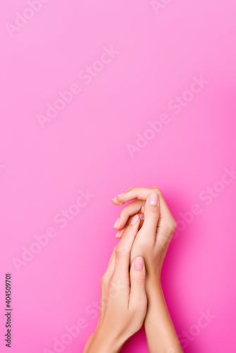 top view of female hands with fingernails covered with pastel enamel on pink background