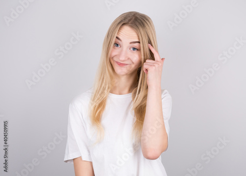 Portrait of young woman thinking with her finger to her head isolated over grey background