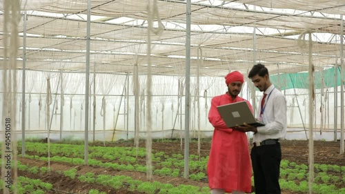 Young indian agronomist showing some information to farmer in laptop at greenhouse
