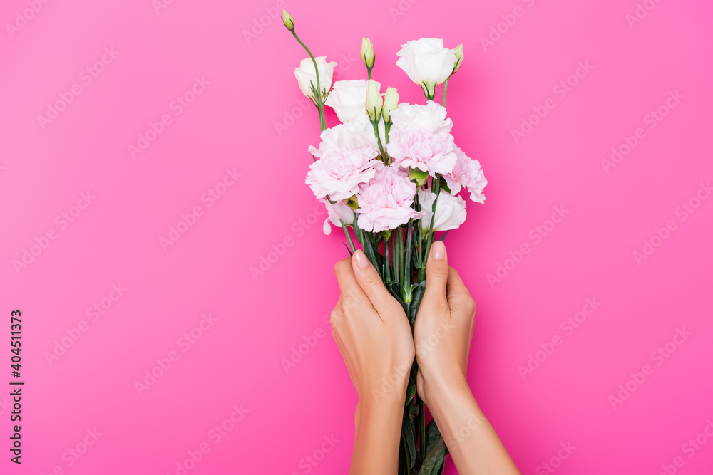 partial view of woman holding carnation and eustoma flowers on pink background