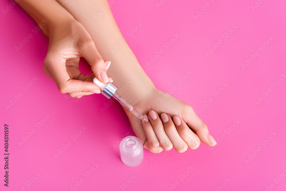 partial view of woman applying cuticle remover with dropper on pink background partial view of woman applying cuticle remover with dropper on pink background