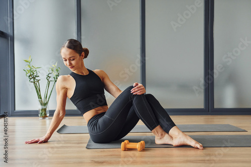 Sits on the mat. Young woman in sportive wear and with slim body have fitness yoga day indoors