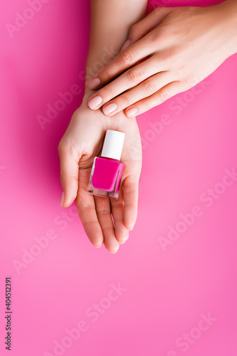 cropped view of woman with bottle of shiny nail varnish on pink background