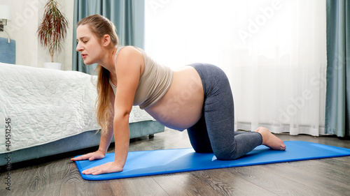 Beautiful pregnant woman stretching and doing yoga exercises on fitness mat at bedroom. Concept of healthy lifestyle, healthcare and sports during pregnancy © Кирилл Рыжов
