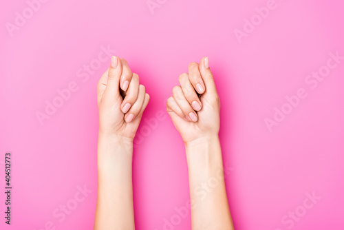 Fényképezés top view of female hands with pastel nail varnish on fingernails on pink backgro