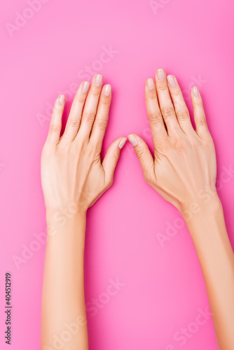 top view of female hands with pastel enamel on fingernails on pink background