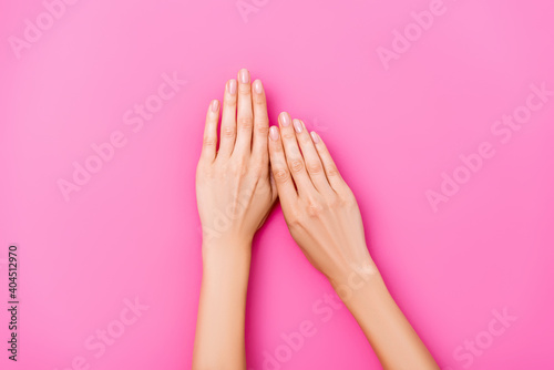 Canvas Print top view of female hands with pastel enamel on fingernails on pink background