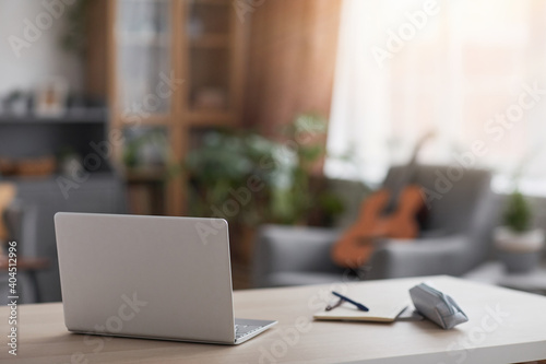 Minimal image of laptop computer on desk in teenage boys room, blurred guitar in background, copy space