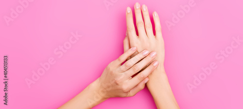 top view of female hands with pastel nail polish on nails on pink background, banner