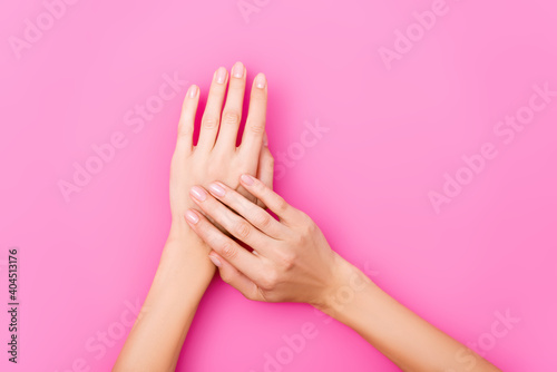 top view of female hands with pastel nail polish on fingernails on pink background