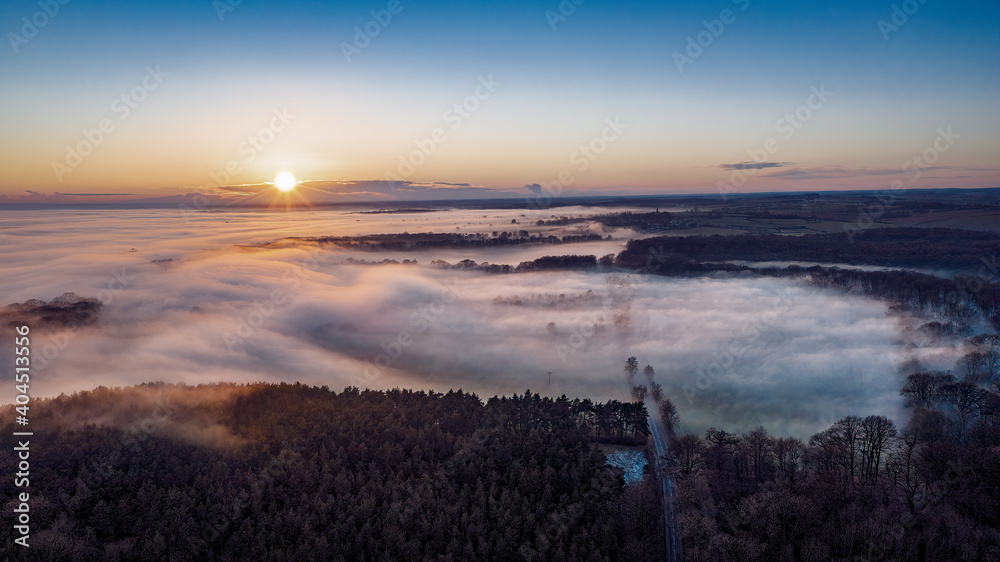 Fototapeta premium Sunset over fog filled trees and road