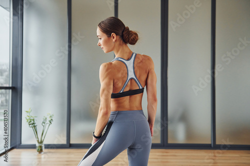 Rear view. Young woman in sportive wear and with slim body have fitness yoga day indoors