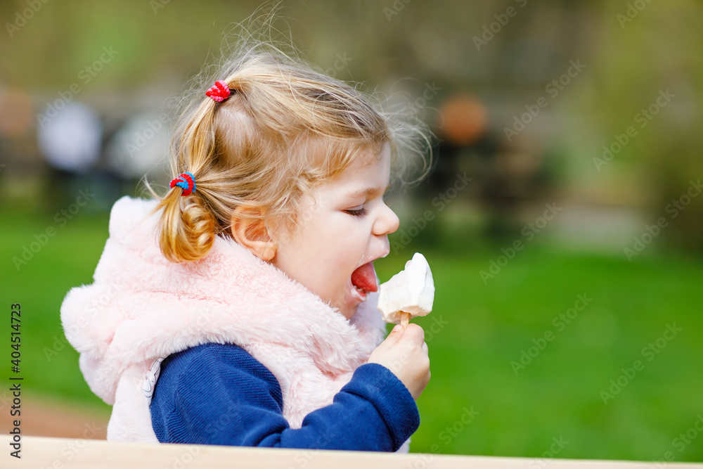 Adorable toddler girl eating sweet ice cream popsicle. food, child, feeding and development concept. Cute happy healthy baby daughter on sunny day outdoors Adorable toddler girl eating sweet ice cream popsicle. food, child, feeding and development concept. Cute happy healthy baby daughter on sunny day outdoors