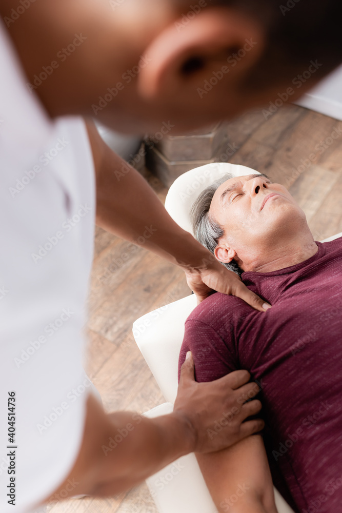 © LIGHTFIELD STUDIOS - blurred african american chiropractor massaging arm of middle aged man on massage table