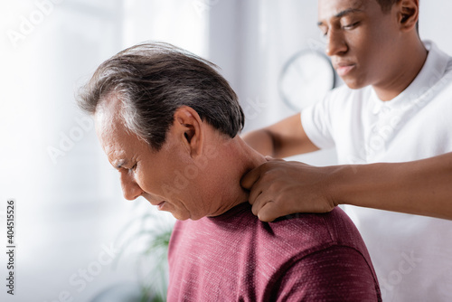 african american physiotherapist massaging middle aged man in clinic