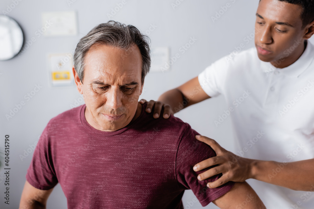blurred african american physiotherapist working with mature man in clinic