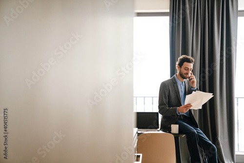 Pleased businessman talking on mobile phone while examining documents