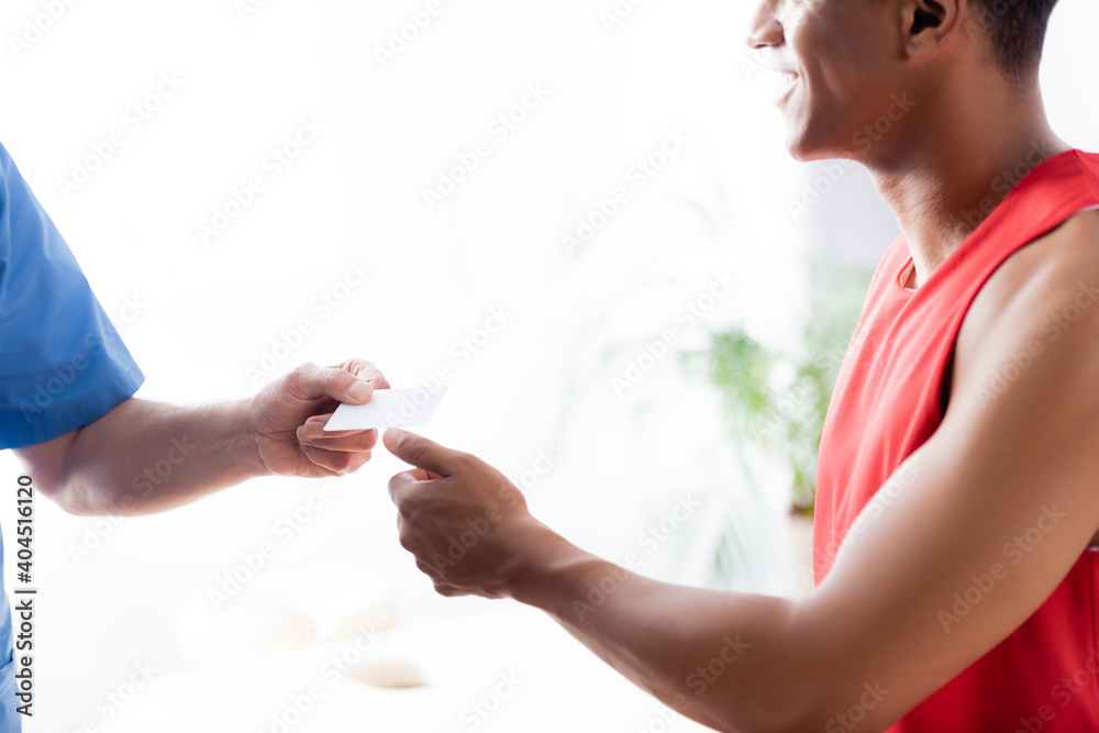 cropped view of doctor giving blank card to cheerful african american sportsman