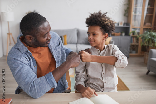 Portrait of African-American father fist bumping smiling son while doing homework together at home photo