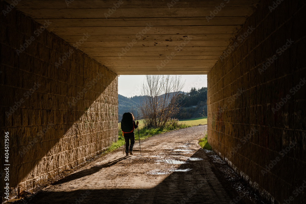 Una pellegrina cammina lungo un sentiero del cammino francese passando sotto ad un ponte