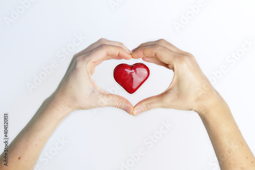 Red love heart levitating inside female hands in the form of a heart against white background. Love concept.